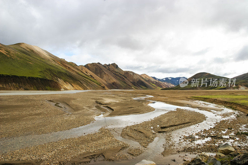 冰岛Laugevegur步道起点的Landmannalaugar周围引人注目的山景，显示了洪水平原上的冰川径流河