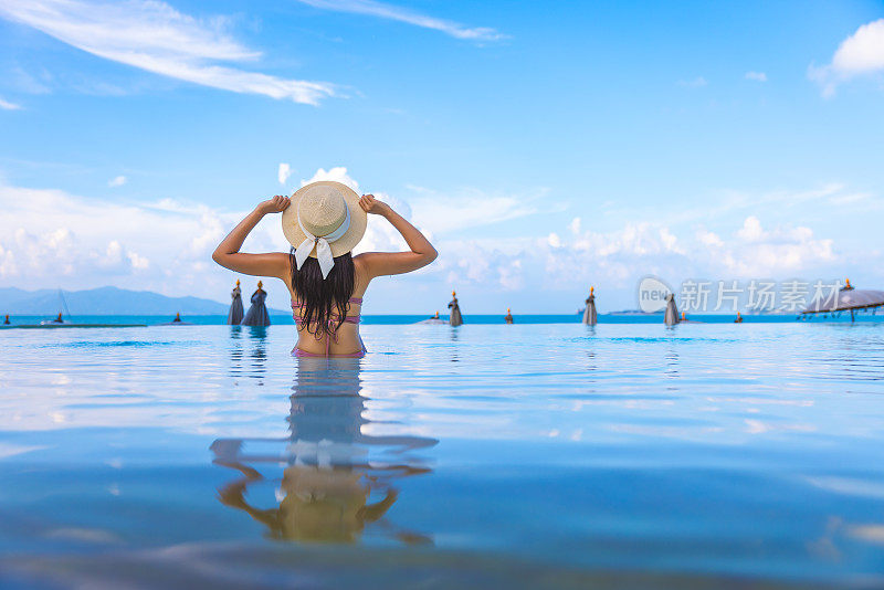 亚洲游客比基尼女子放松和旅行在泰国苏梅岛海滩的无边泳池度假村