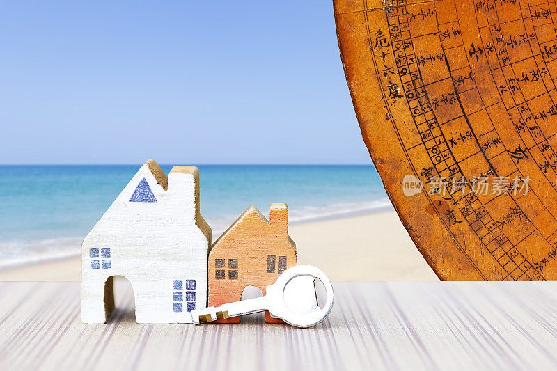 迷你房子，钥匙和古老的中国风水罗盘板在模糊的海滩背景