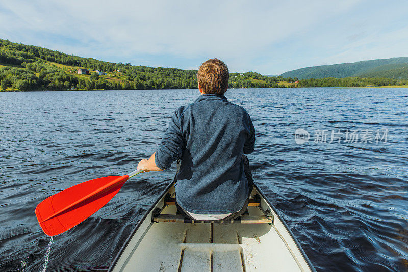 男子在挪威风景优美的湖泊上划艇的后视图