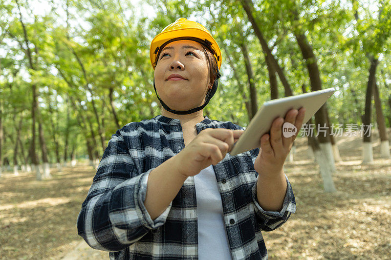 戴着头盔、穿着安全背心的女工程师在平板电脑上做笔记