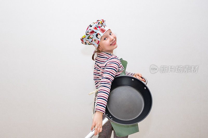 一个白人女孩，8岁，打扮成厨师，手里拿着一只大煎锅。女孩微笑着拿着煎锅摆姿势。