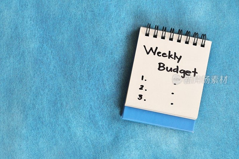 每周预算概念。白色的记事本孤立在蓝色的背景。