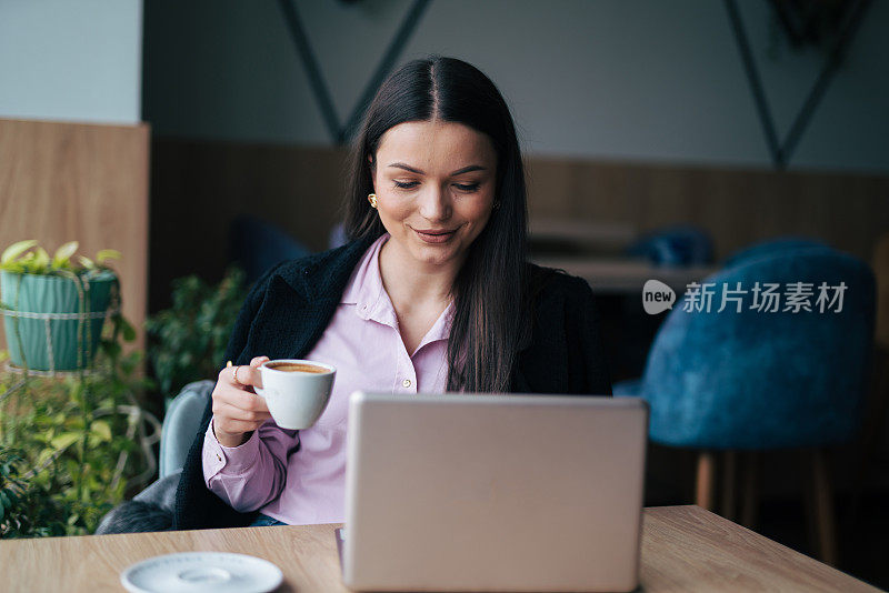 一个漂亮的年轻女人拿着笔记本电脑和一杯咖啡坐在咖啡馆里