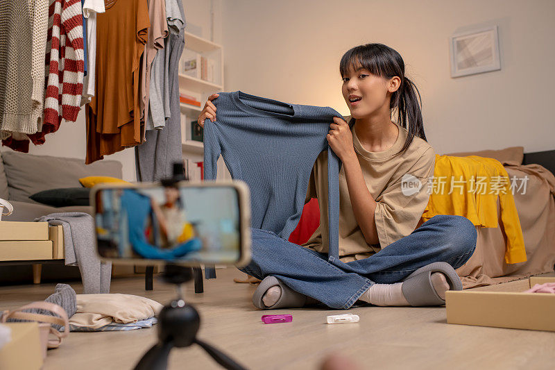 年轻的亚洲女性企业家沉浸在她的副业中，在舒适的家中直播和销售时尚服装。在她的空闲时间致力于建立一个企业和创造时尚的网上购物