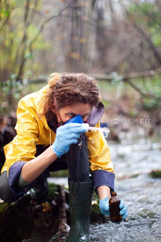 集中的高加索女性环境生物学家从一条溪流中收集水样作进一步检查
