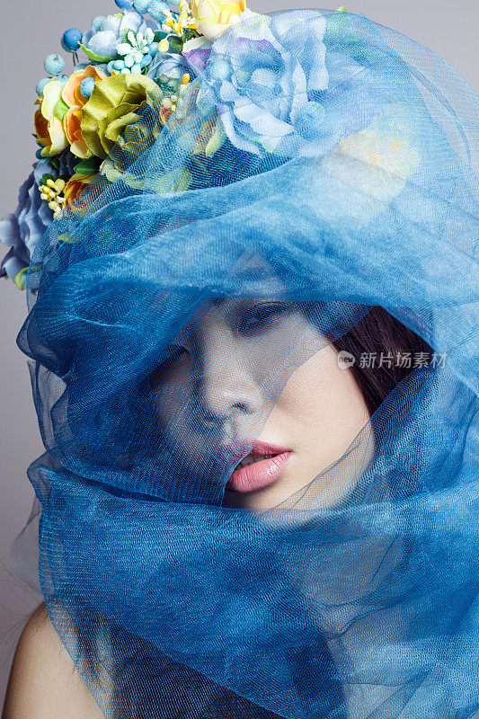 神秘美丽的女人带着花帽子，女性化着妆，用蓝色的面纱遮住她的脸。