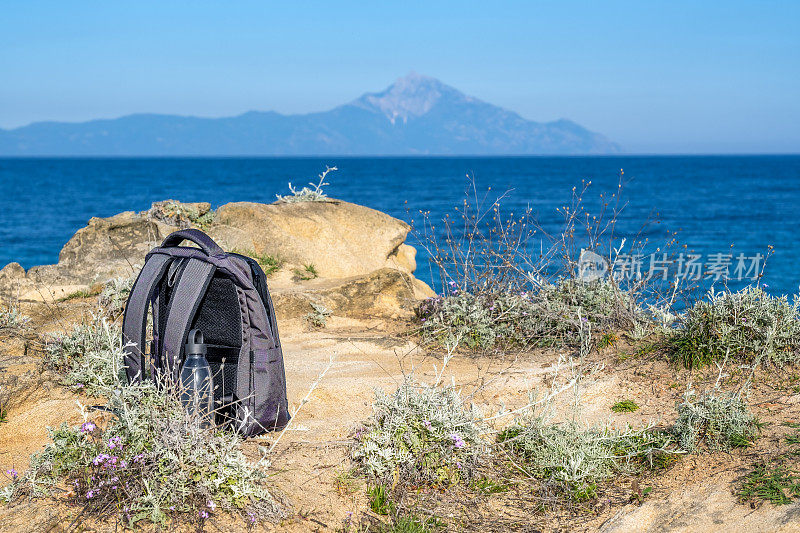 哈尔基季基上,阿托斯景观春季徒步旅行在你。背包和可重复使用的塑料瓶放在海滩附近的岩石上