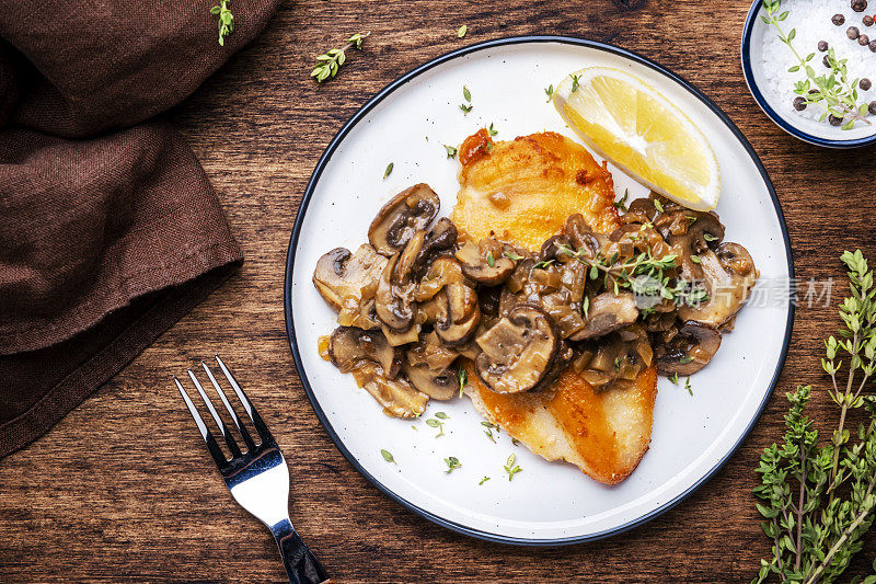 法式面包屑鸡肉牛排配蘑菇和洋葱酱配白葡萄酒，柠檬和百里香，质朴的餐桌背景，俯视图