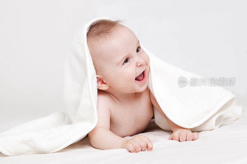 可爱的婴儿在白色的毯子下微笑