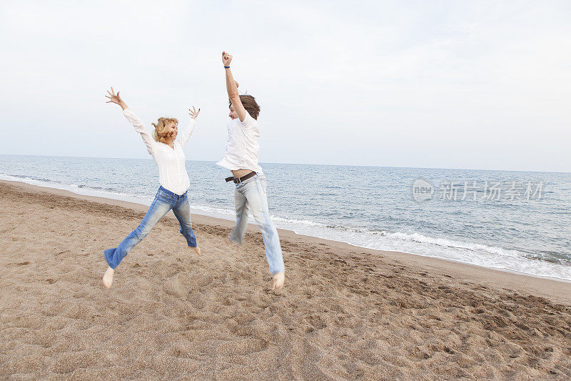 年轻夫妇在海滩上举着手臂跳跃