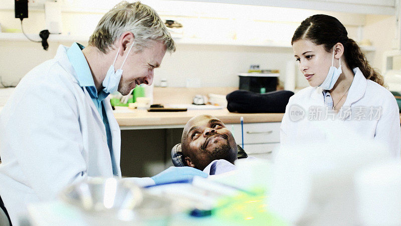 微笑的牙医安抚病人，他的助手看着