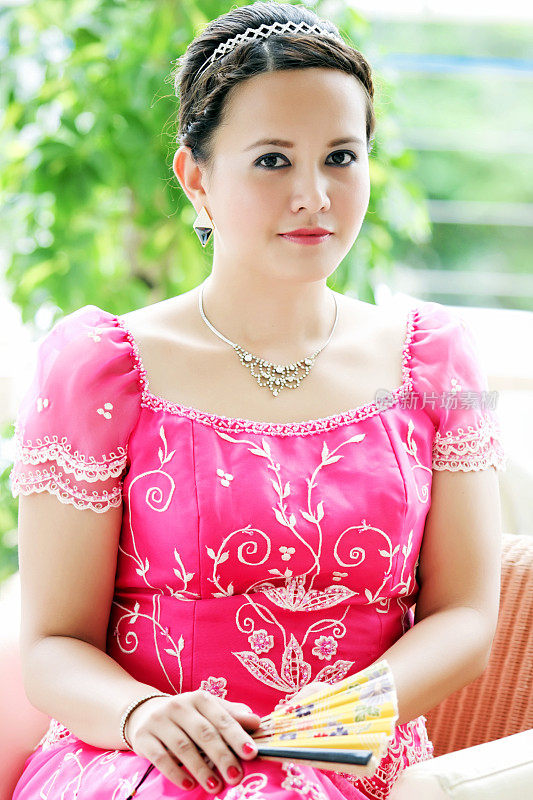 年轻的亚洲女人穿着粉红色的衣服，拿着一把黄色的扇子