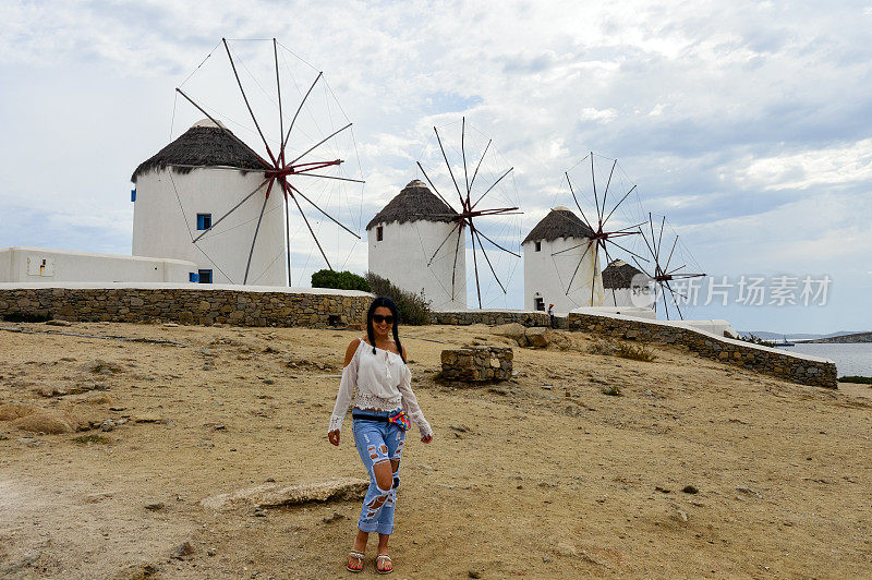 美丽的女孩摆姿势的风车米科诺斯，希腊