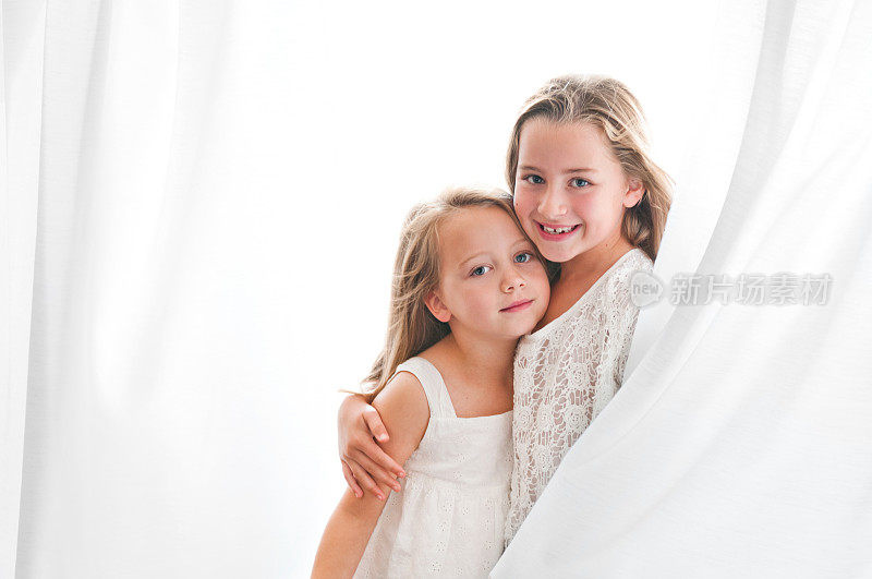 姐妹们在白色窗帘和明亮的背景中玩耍