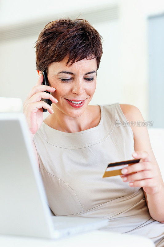 成熟的商业女性用信用卡购物和用手机聊天