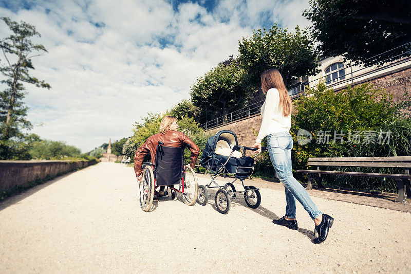 年轻的父母坐着轮椅推着婴儿车在公园里