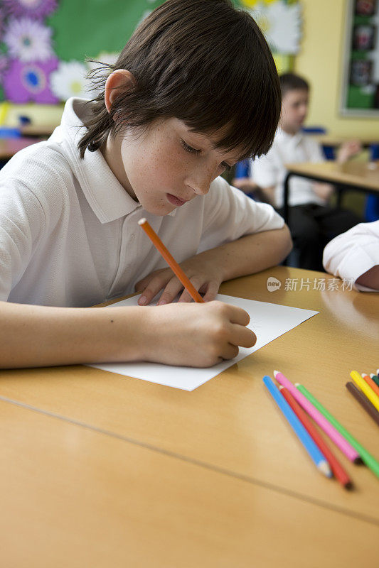 一个男孩在学校用彩色铅笔在书桌前画画。