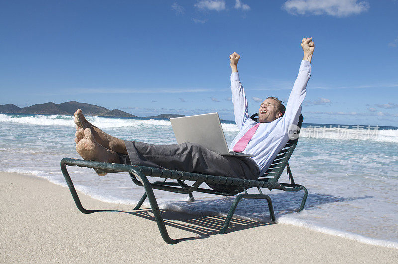 商人在沙滩椅上用笔记本电脑庆祝