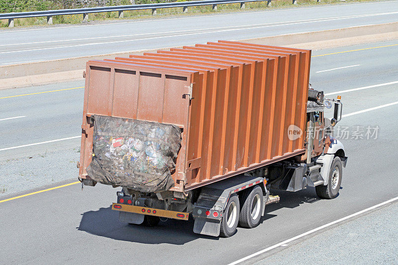 一辆卡车在高速公路上拖着一个工业垃圾桶