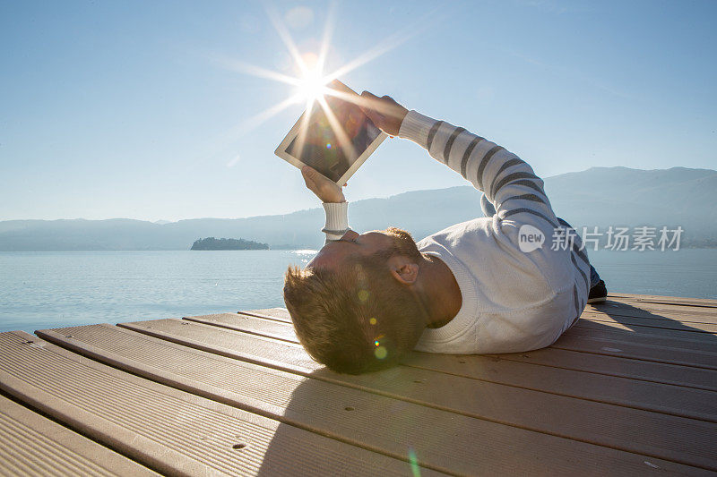 一个年轻人在湖边的码头上玩着平板电脑