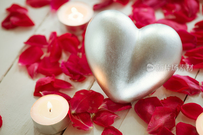 银色的心与蜡烛和红玫瑰花瓣装饰