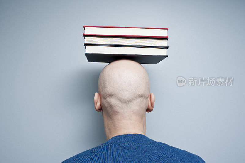 秃顶男人的后视图，头上顶着三本书。