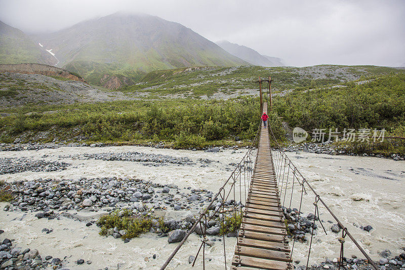 背包客在横跨阿拉斯加河的吊桥上徒步旅行