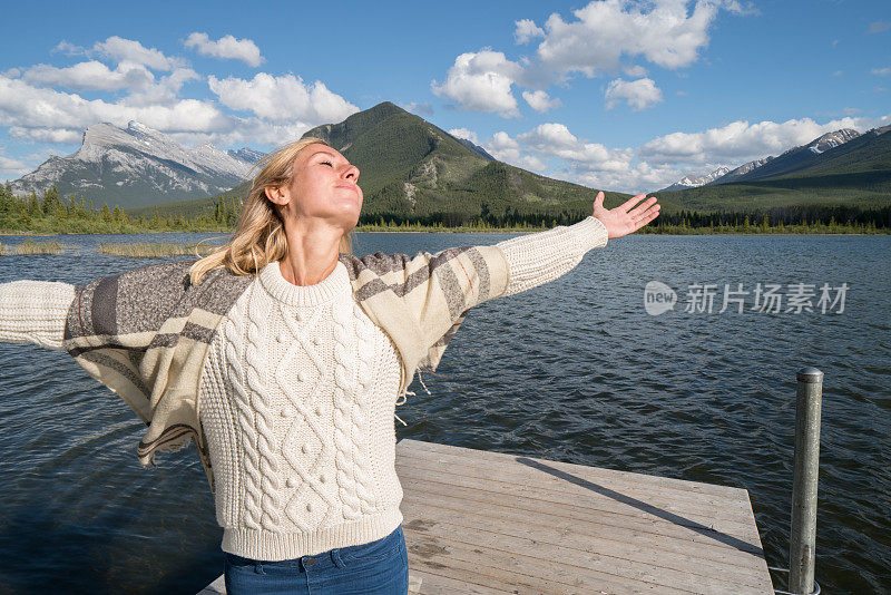 年轻女子在湖边的码头上张开双臂