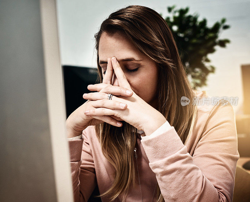 坐在电脑前的金发女子双手合十，闭上眼睛