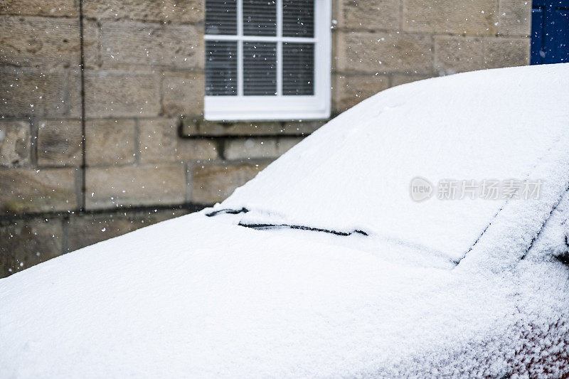 汽车的挡风玻璃上覆盖着积雪，停在城市的街道上。