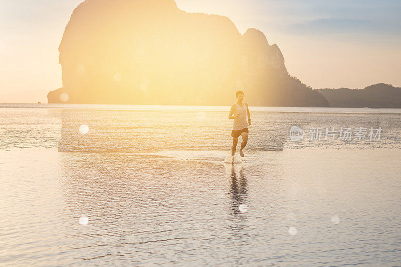 年轻的亚洲男子在海滩上奔跑，夕阳为背景