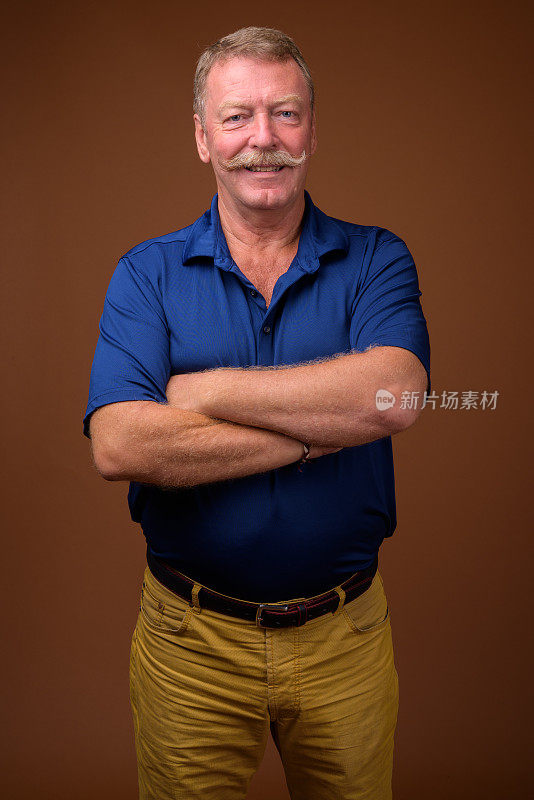 工作室拍摄的英俊的老男人与胡子穿着蓝色马球衬衫对彩色背景