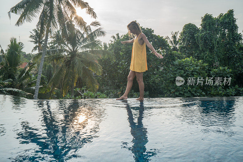 年轻女子走在一个热带天堂目的地的游泳池边缘;女游客在旅游度假池享受度假乐趣的概念