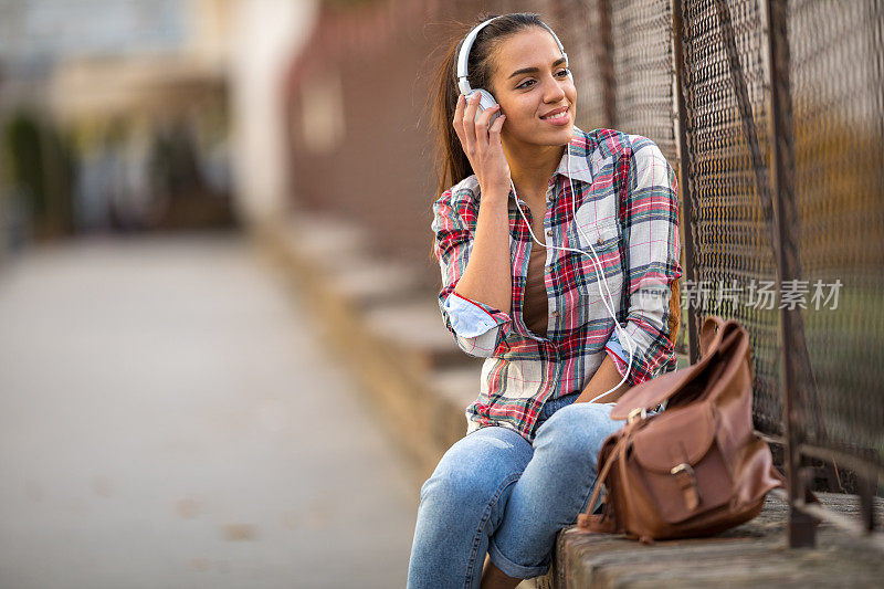 美丽的年轻女子在街上听音乐