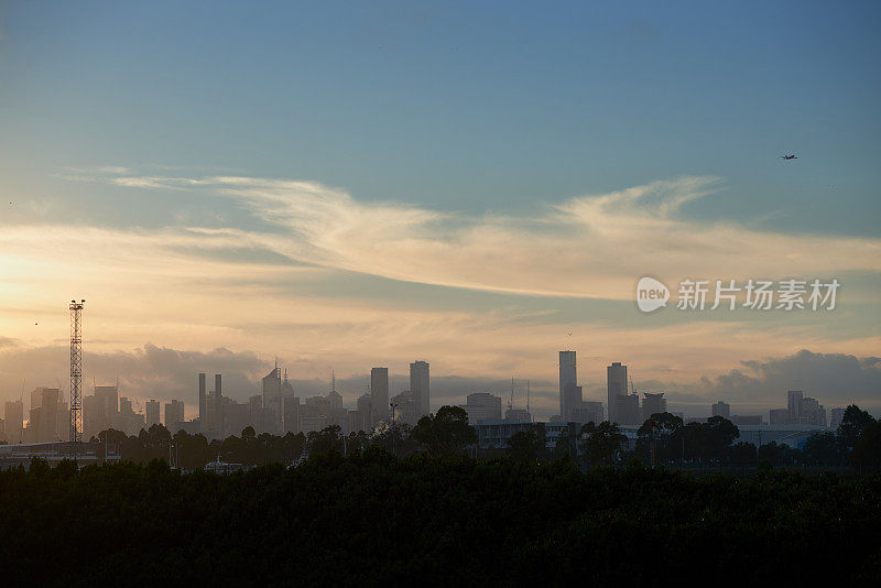 墨尔本城市的天际线在一个朦胧的晨光和一架飞机在天空。