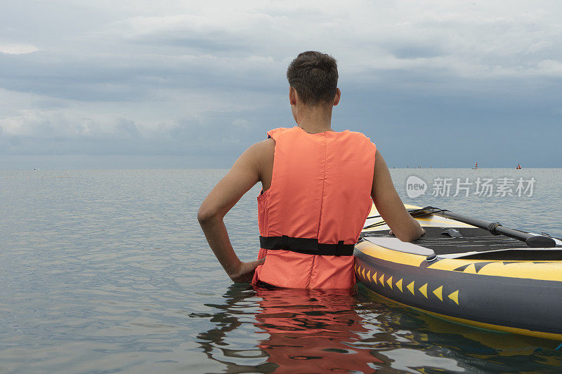 穿着救生衣的冲浪人正准备冲浪。一个年轻人在海滩上带着冲浪板。冲浪者和海洋。水上安全