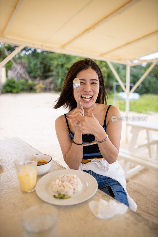 快乐的年轻女人在度假海滩用勺子做鬼脸