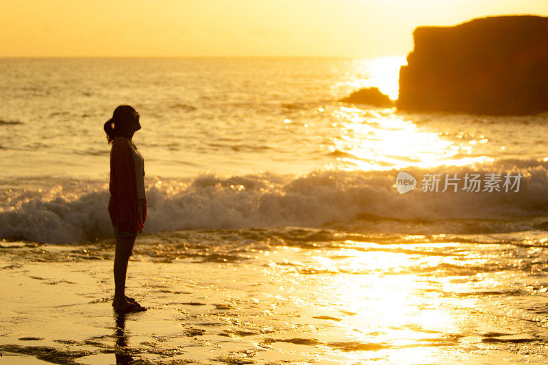 亚洲女人站在海边的海滩在日落