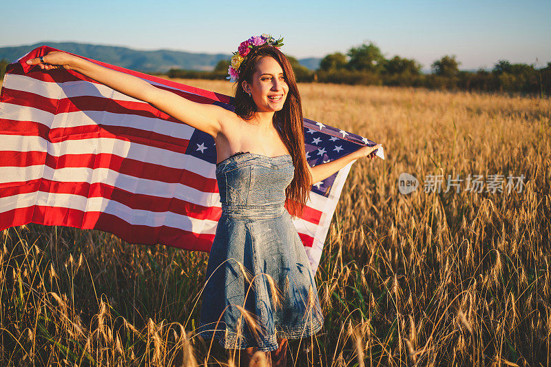 一位年轻女子举着美国国旗站在麦田里