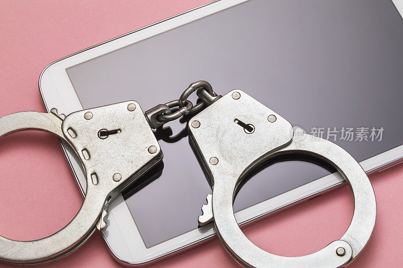 粉色背景上的手铐和平板电脑。计算机犯罪刑罚概念