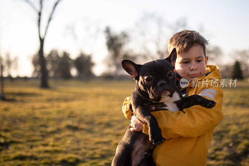 在公园里，一个男孩抱着一只法国斗牛犬，通过嘴唇叹气