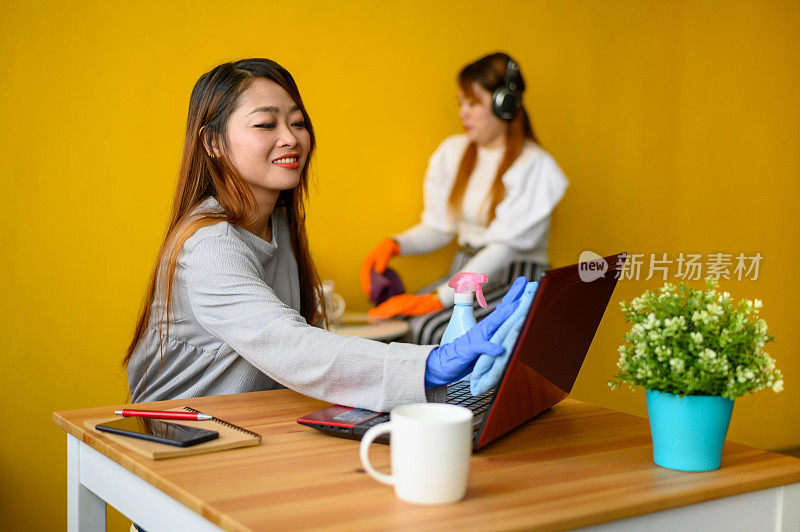 新冠肺炎大流行期间，年轻亚洲女性在办公室使用消毒剂消毒笔记本电脑表面