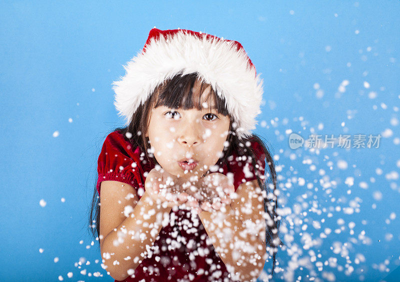 亚洲小女孩戴着圣诞老人的帽子吹雪花