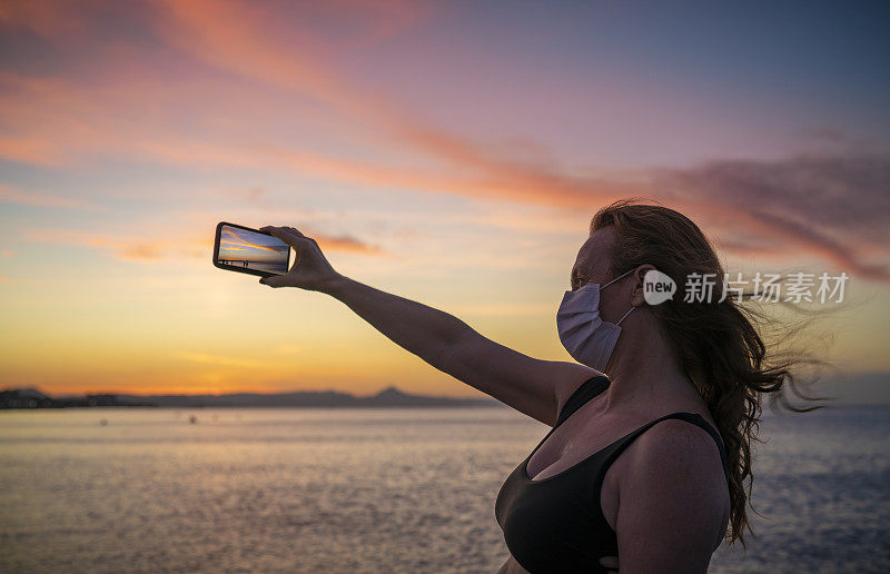 游客50岁的成年妇女在日落海滩戴口罩拍照