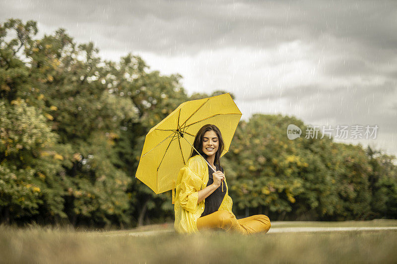 美丽的年轻女子穿着黄色雨衣，拿着黄色雨伞在户外