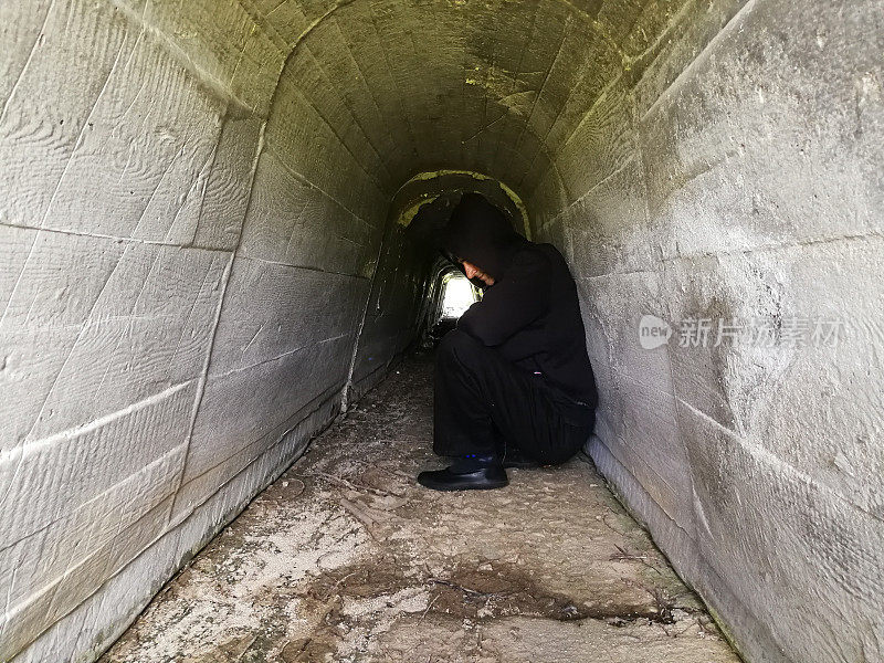 一个沮丧的人坐在黑暗的隧道里等待光明的到来