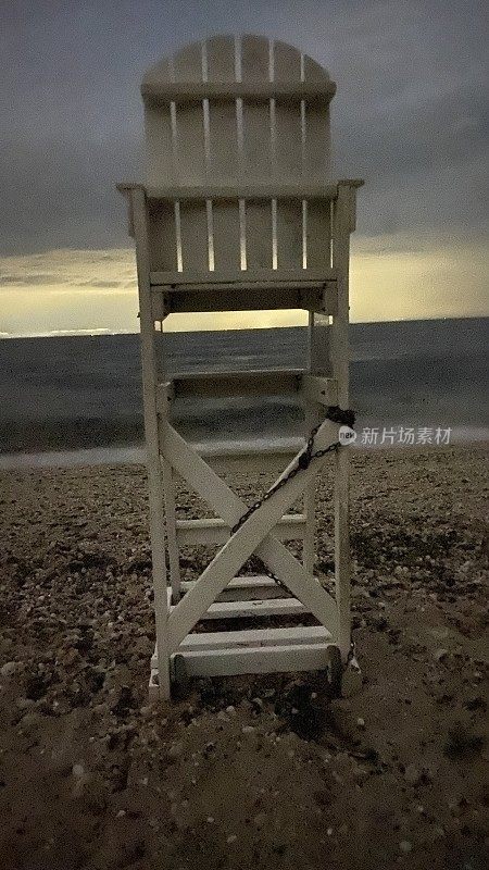 在阴沉沉的黄昏天空下的海滩上的救生员椅子