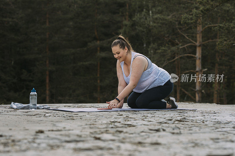 远离城市:胖女人用手机上的应用程序在大自然中做瑜伽