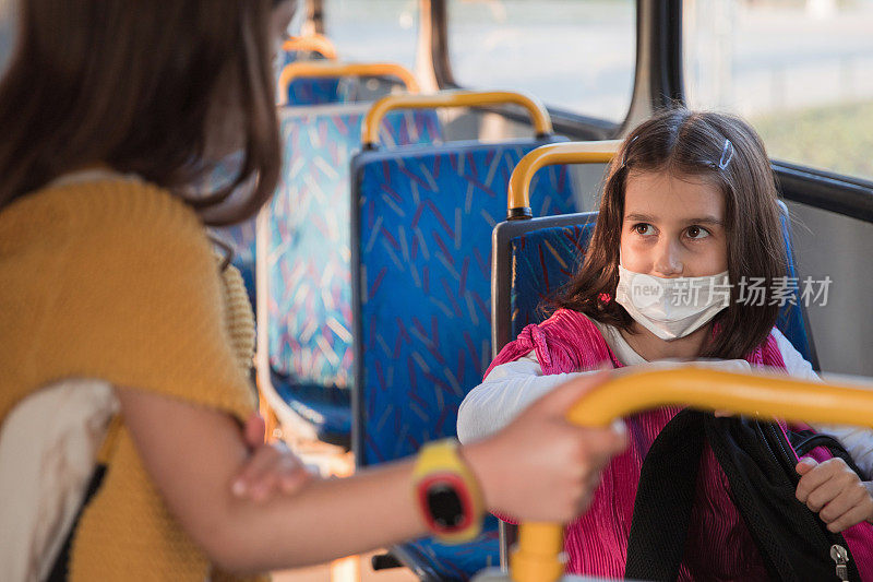 戴口罩的女孩坐在公交车上，腿上放着书包